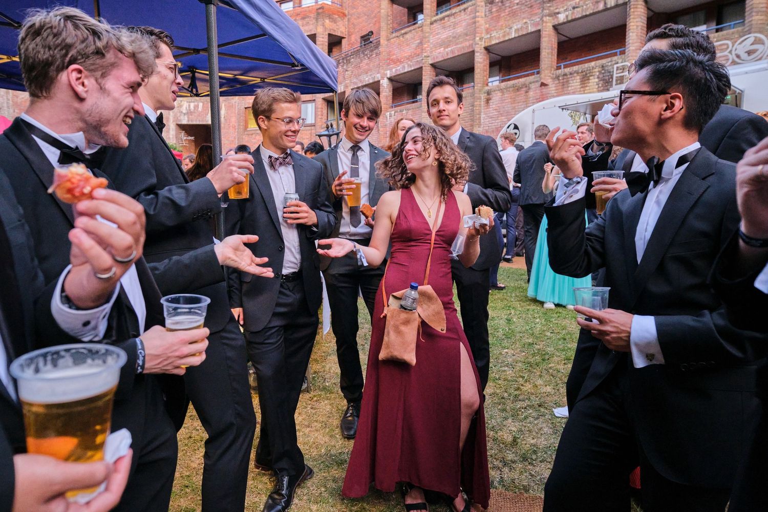 Outdoor reception gathering with guests mingling and holding drinks at dusk.