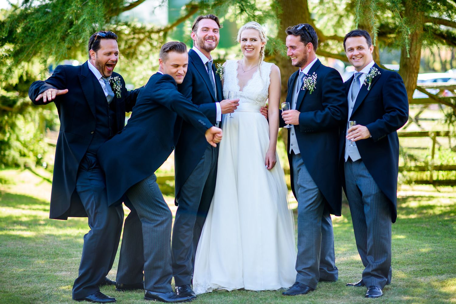 Wedding party striking fun poses and celebrating on the lawn outside.