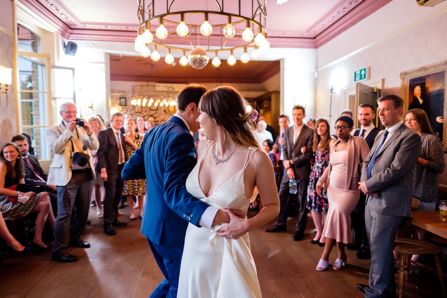 Couple shares first dance at wedding reception as guests watch from sides of room.