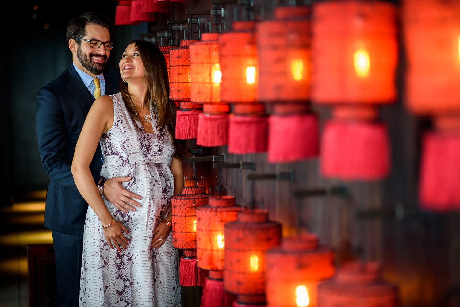 Couple poses against a wall of glowing red Asian lanterns creating romantic ambiance.