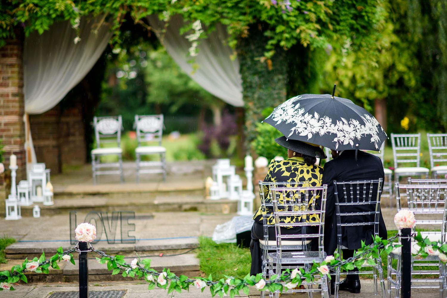 Outdoor wedding venue setup with green foliage and white chairs.