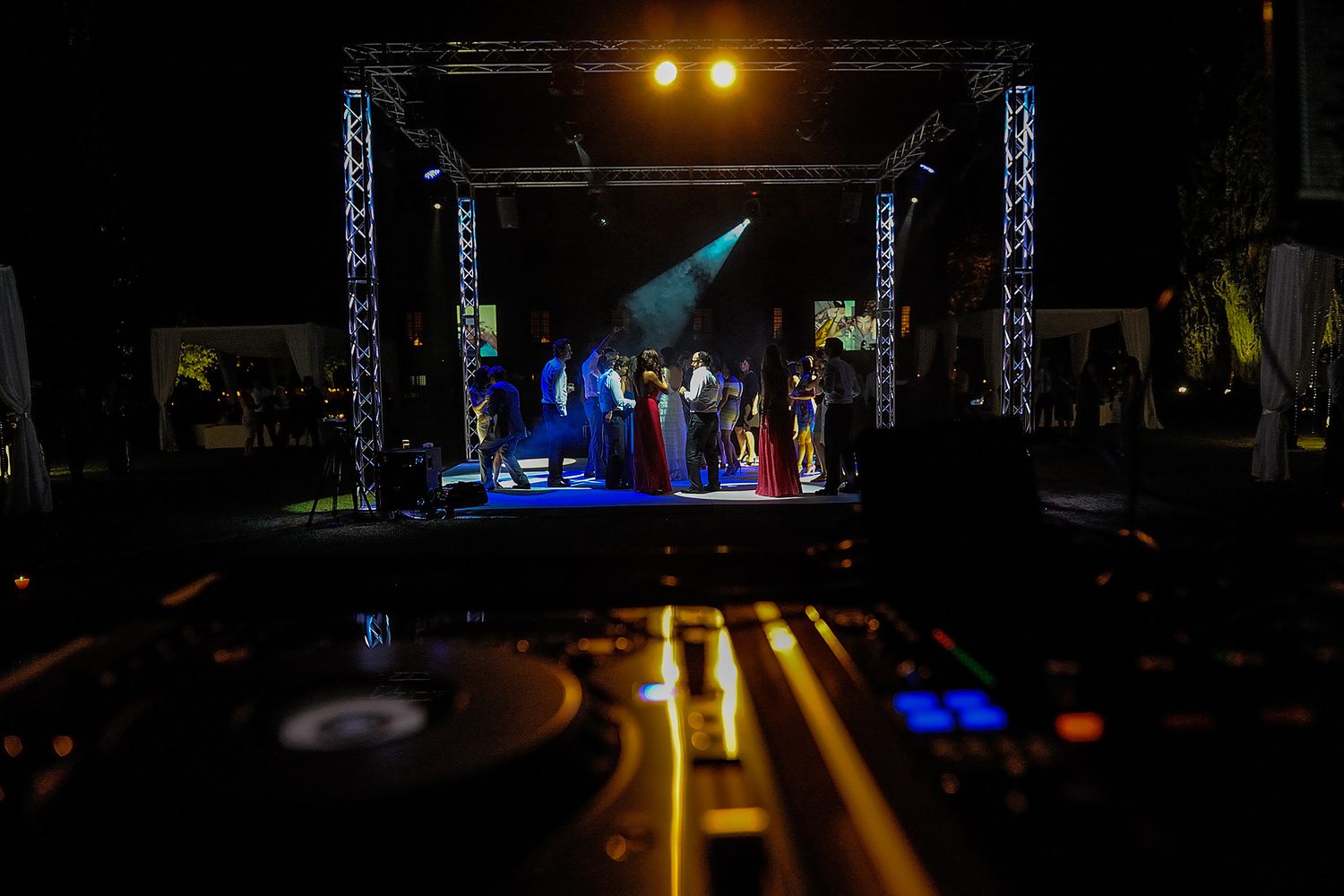 DJ equipment and performers silhouetted on illuminated stage during nighttime concert.