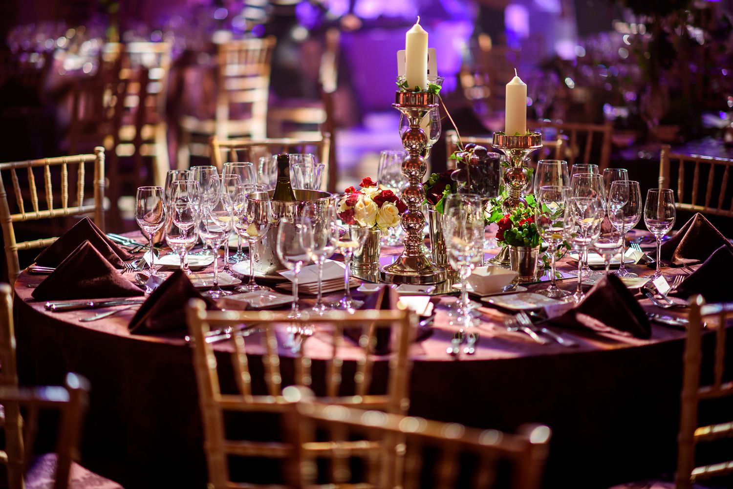 Elegant reception table settings with purple ambient lighting and crystal glassware.