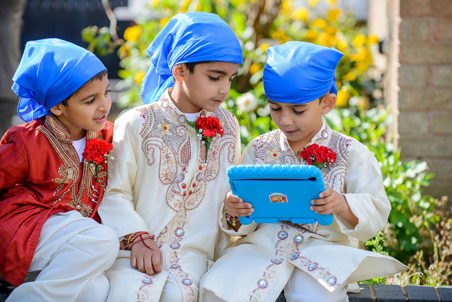 Children in blue caps and traditional Indian outfits sitting together outdoors.