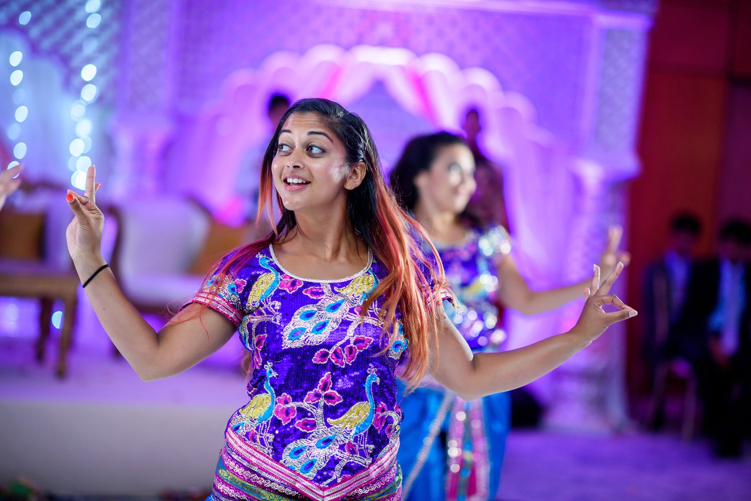 People dancing joyfully at a wedding celebration with purple-tinted lighting and festive atmosphere.