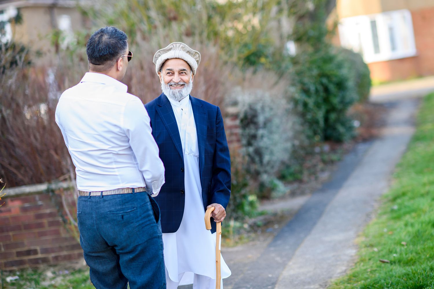 Two people having a conversation on a suburban pathway near brick walls.