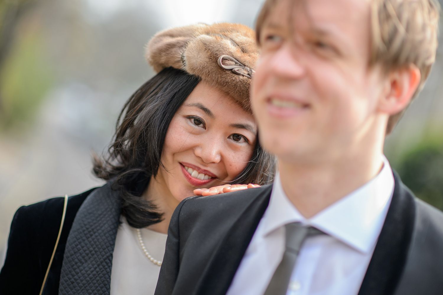 Close-up portrait of a couple in formal attire with one wearing a stylish hat.