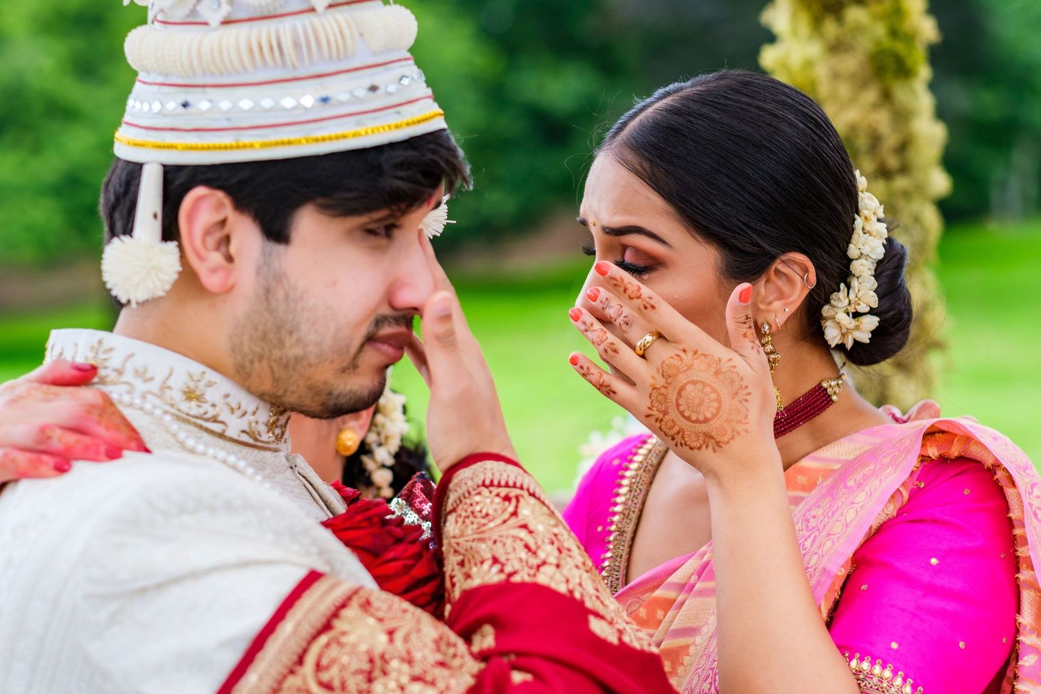 Wedding party celebrates outdoors in traditional South Asian attire with vibrant pink and red colors.