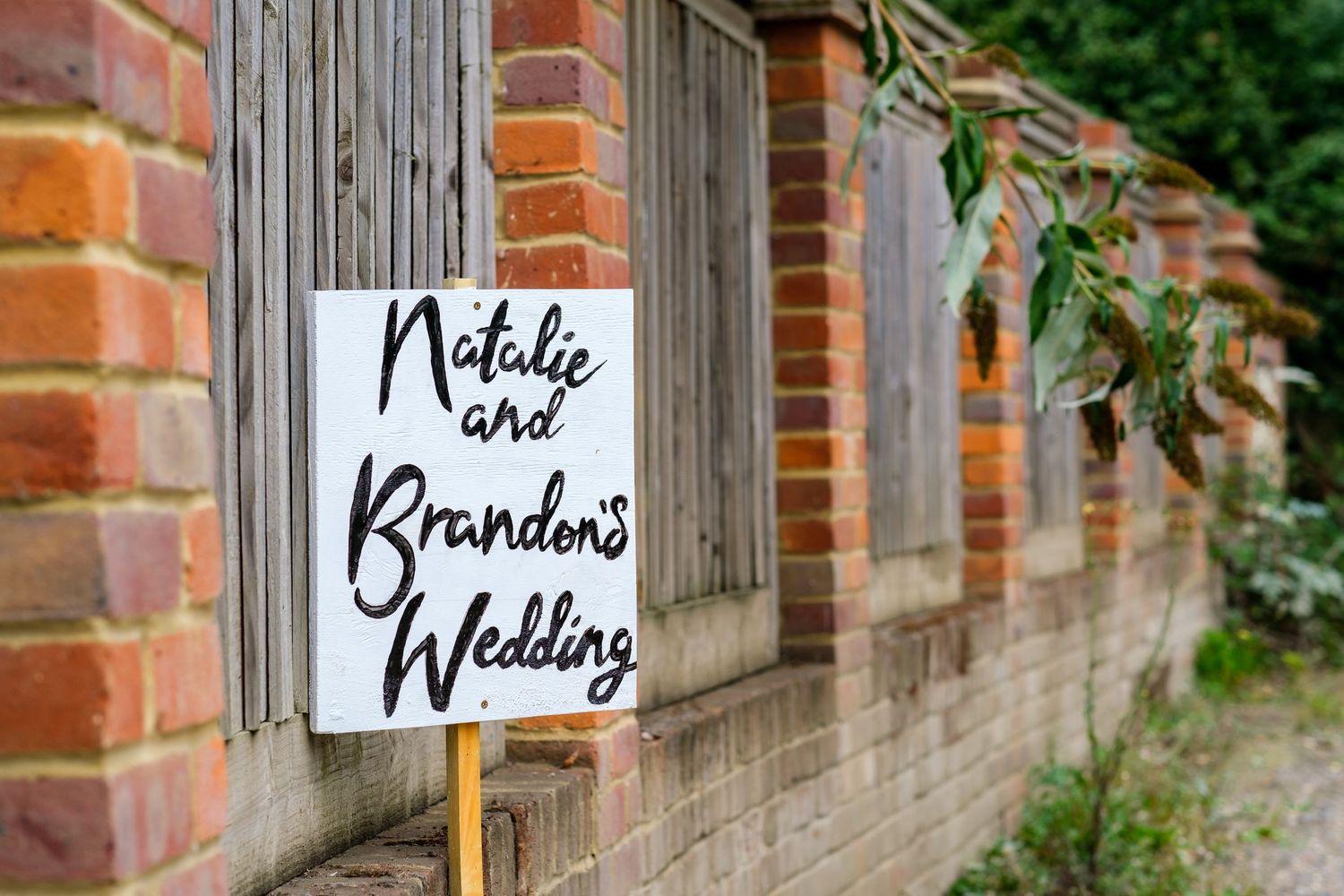 Rustic brick wall with wooden signs directing guests to different wedding areas.