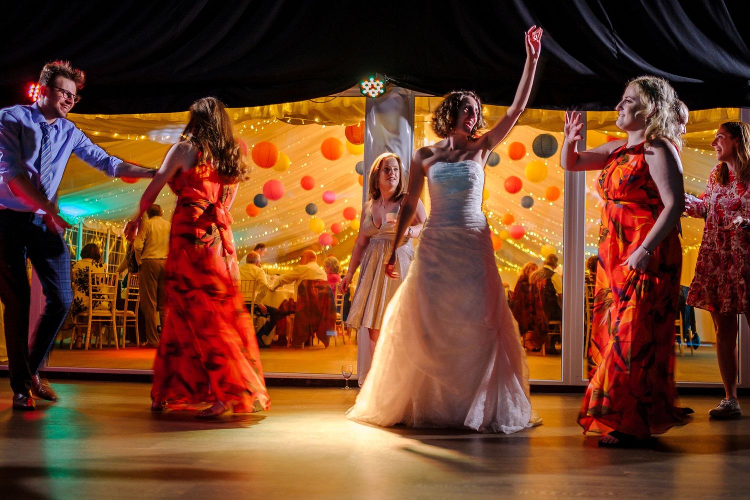 Wedding reception dance floor with colorful lighting and guests in festive attire.