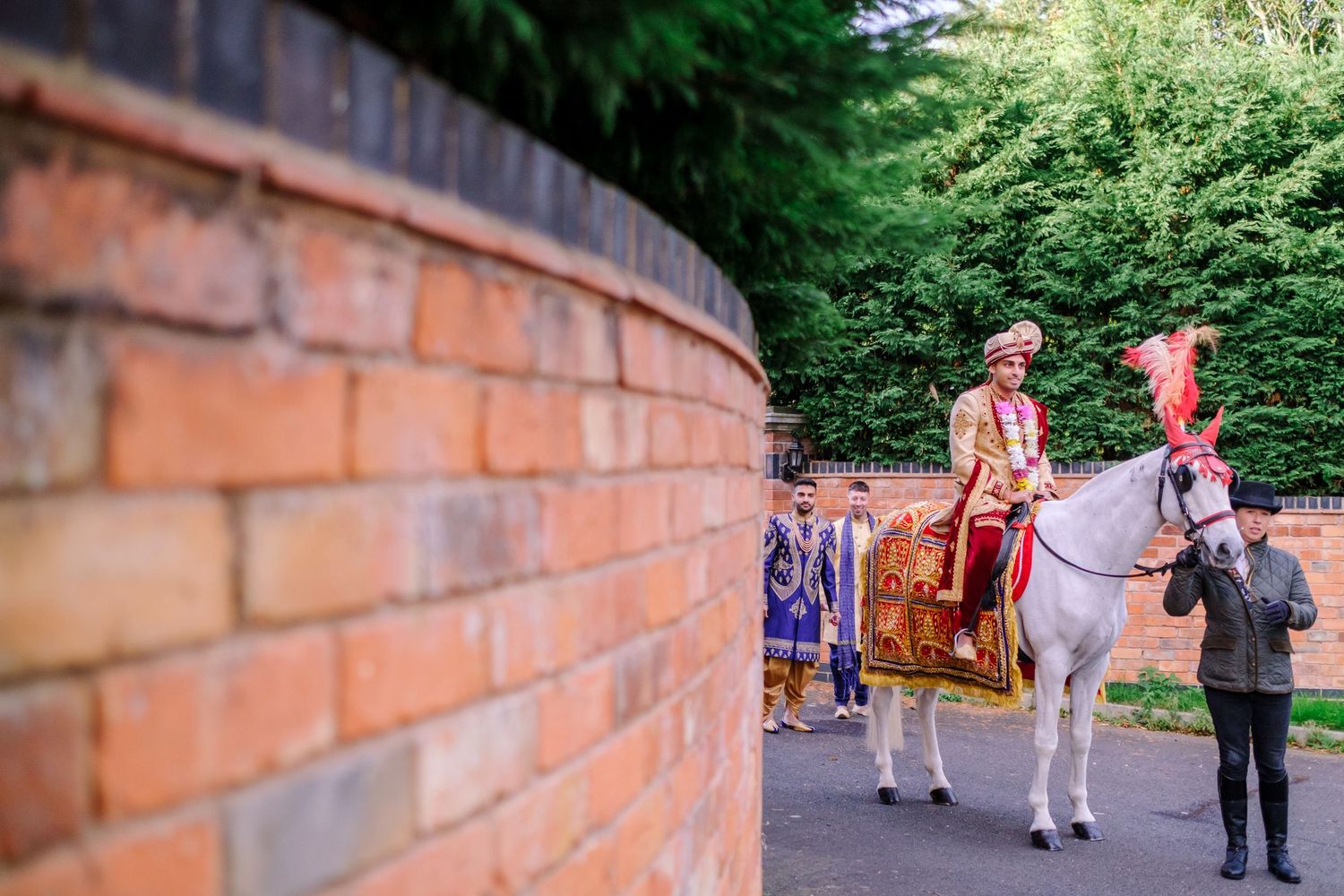 Wedding party walking along a curved brick wall path surrounded by lush greenery.