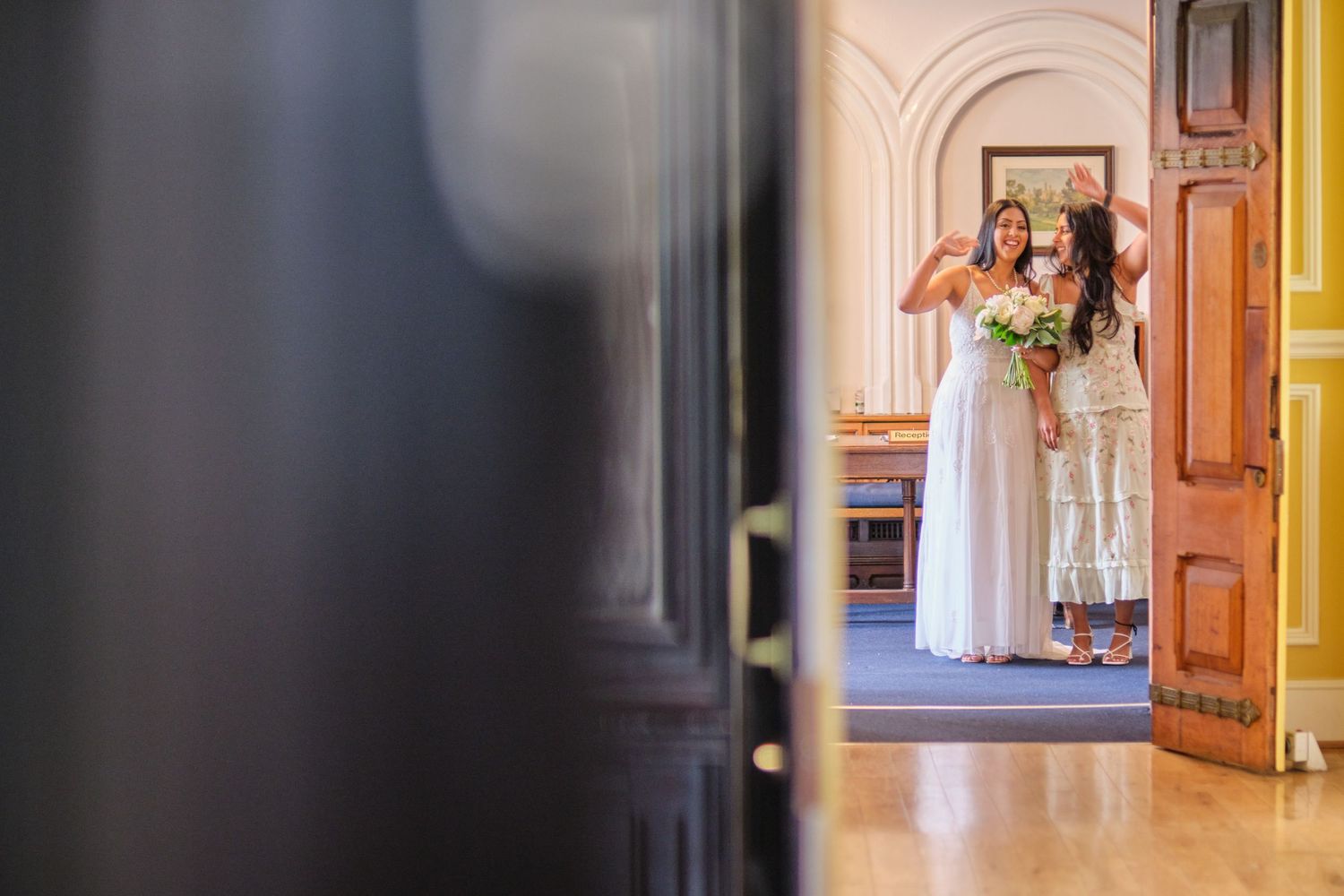 A glimpse through an open doorway shows a figure in white holding a bouquet in an elegant interior hallway.