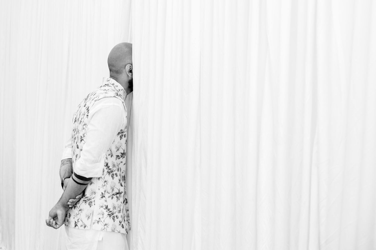 Wedding couple in traditional attire dancing and celebrating against white curtains.