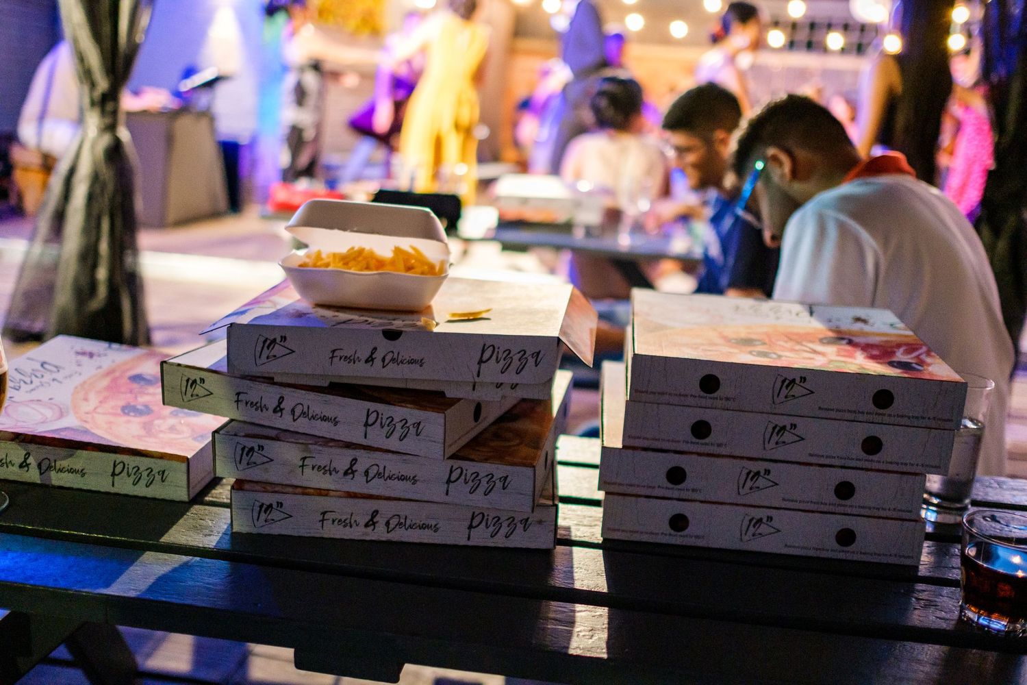 Stacks of pizza boxes lined up on a counter in dim lighting at a restaurant or delivery service.