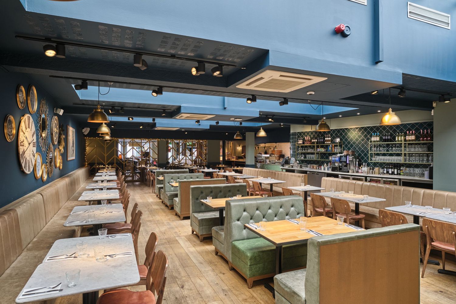 Modern restaurant interior with blue walls, wooden tables and green booth seating in an upscale casual dining setting.