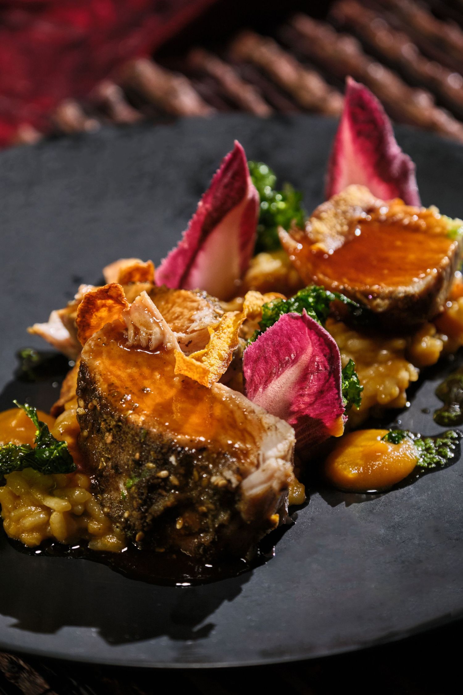 Elegant plated dish with seared fish, roasted vegetables, broccoli, and pink radicchio on a dark slate plate.