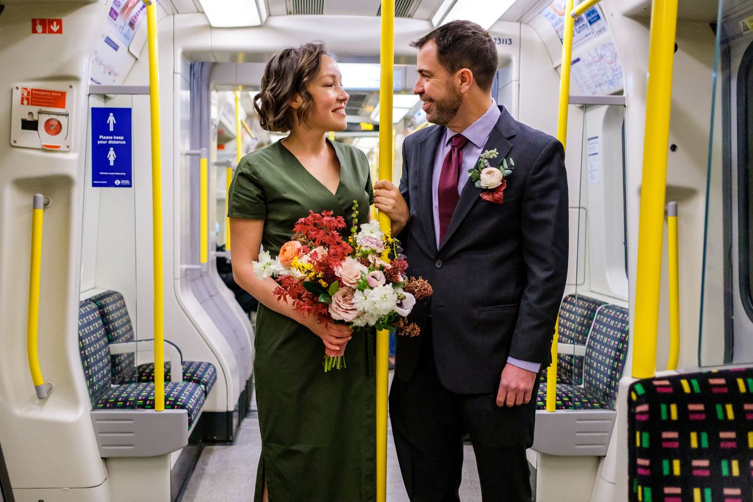 A couple in wedding attire shares a joyful moment while riding on a subway train.