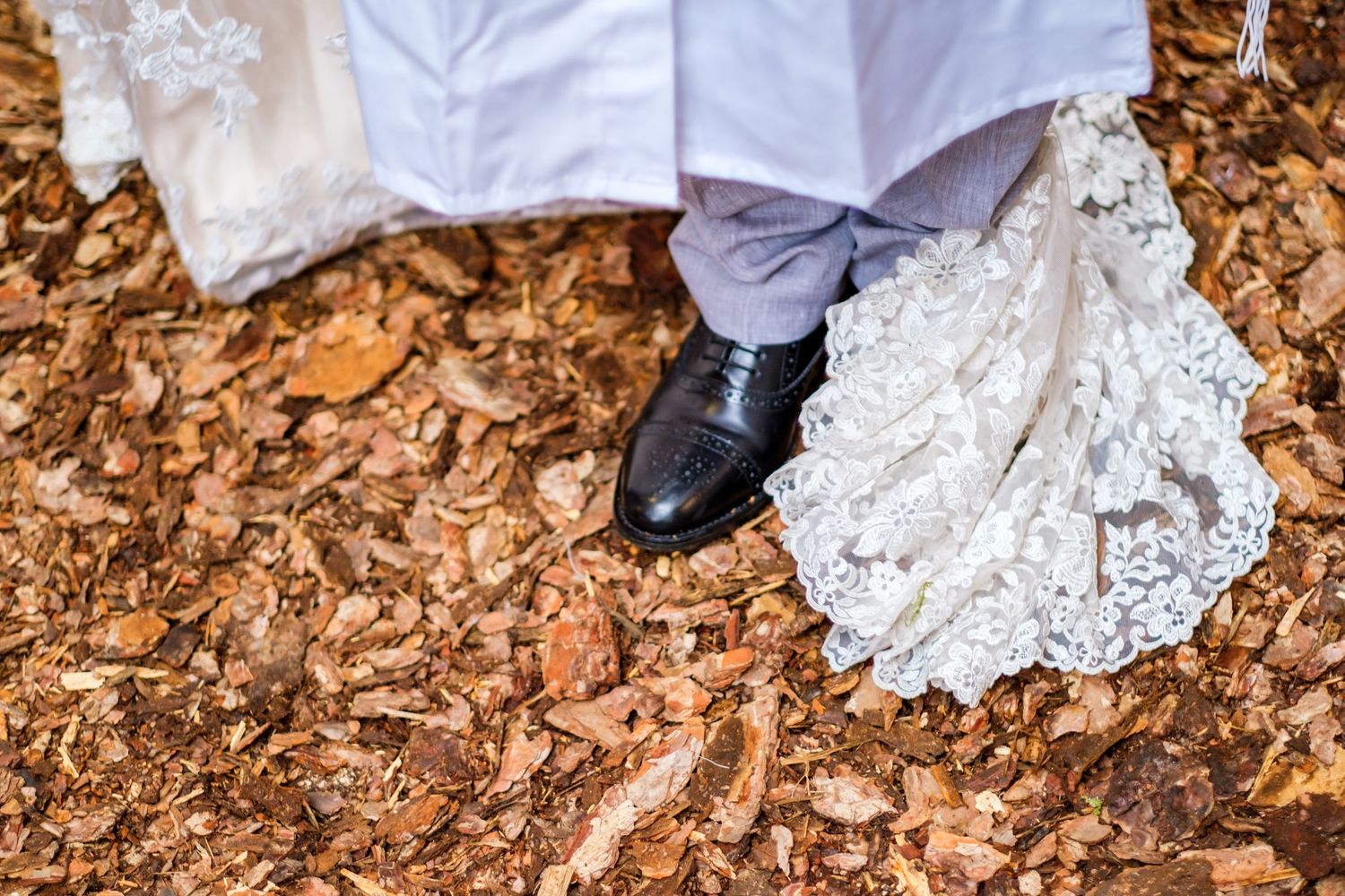 White lace wedding dress details against rustic brown leaves on the ground.