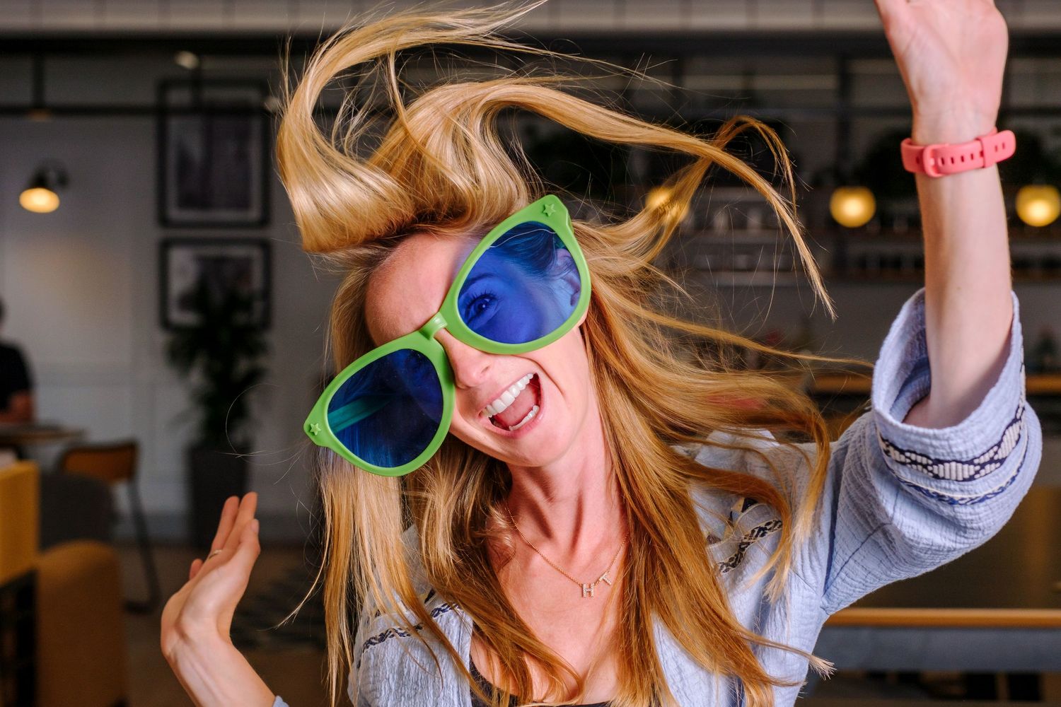Woman wearing bright green sunglasses dances joyfully with blonde hair flowing.