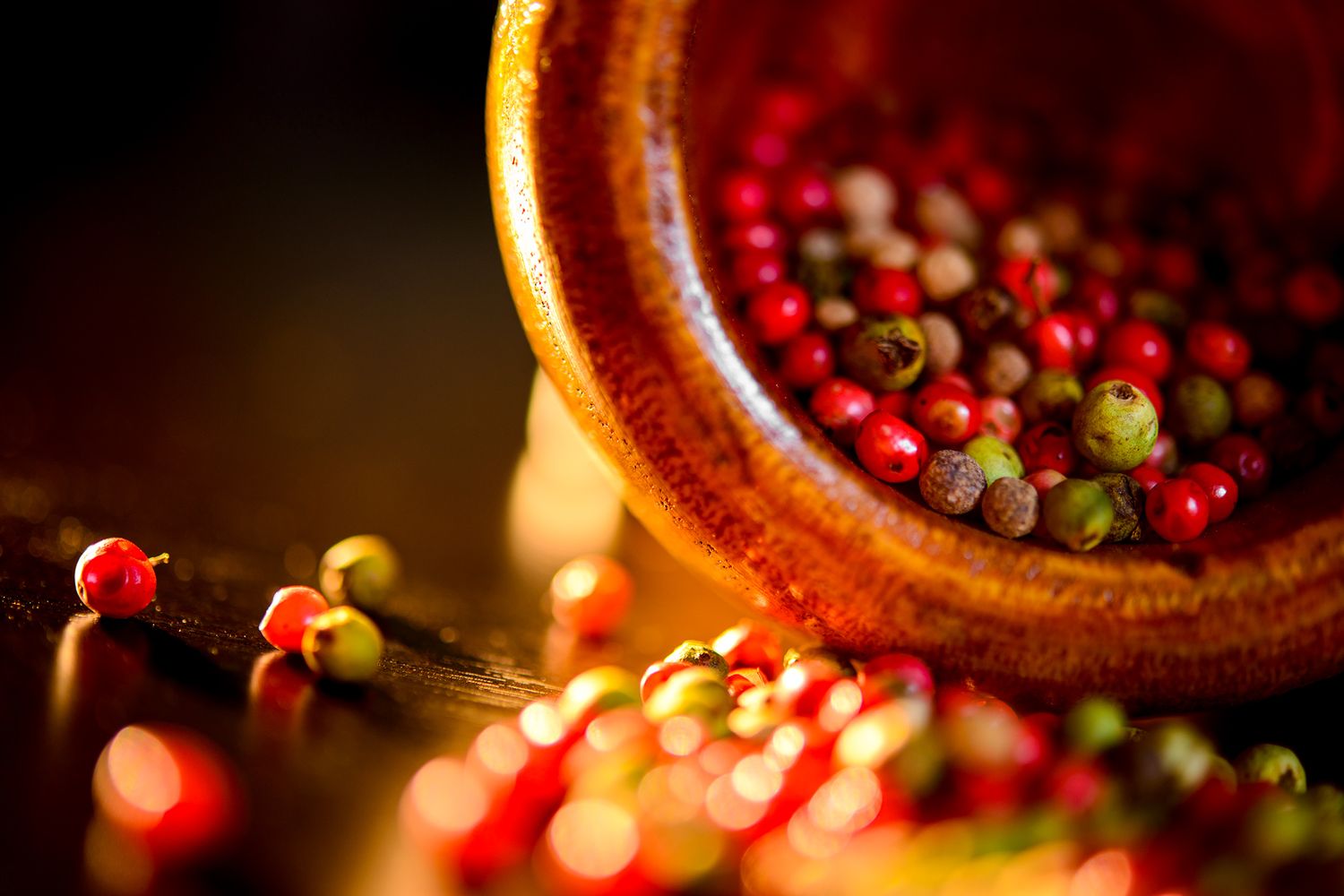 Colorful peppercorns in red, green and pink varieties in a rustic bowl with dramatic lighting.