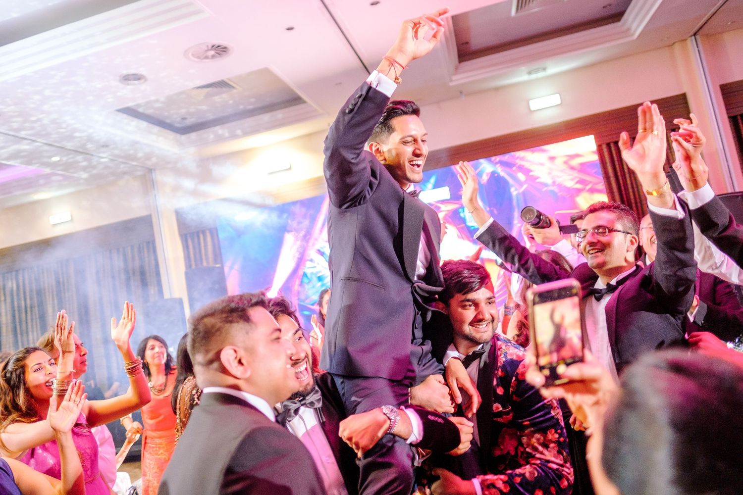 People dancing and celebrating at a lively party with colorful lighting and festive atmosphere.