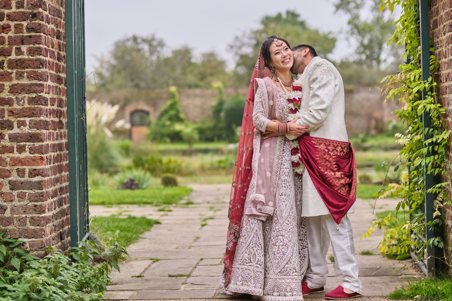 Couple in traditional South Asian wedding attire posing together in a garden setting.