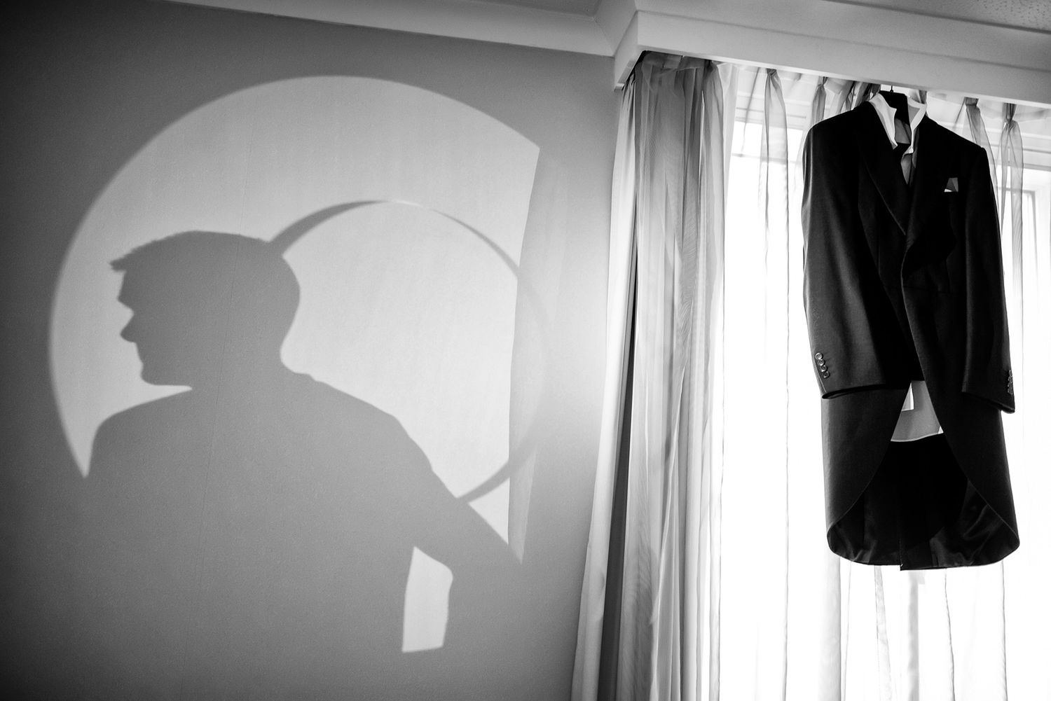 Black and white series of groom getting ready with suit jacket against dramatic lighting.