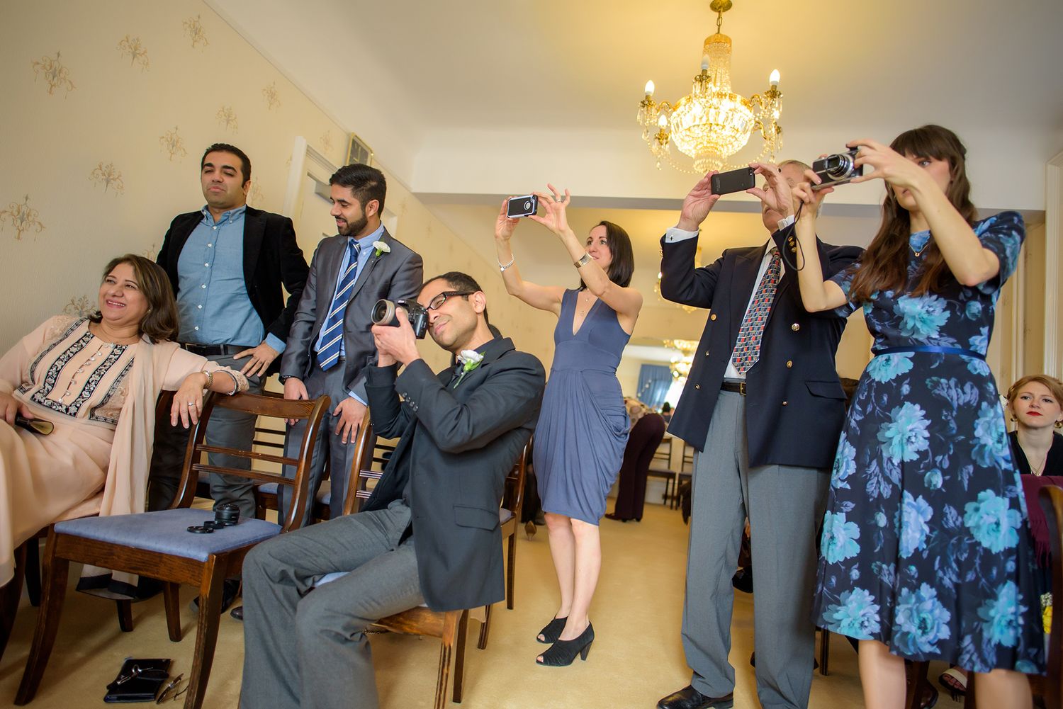 Wedding guests react emotionally during ceremony in a room with chandelier and blue drapes.