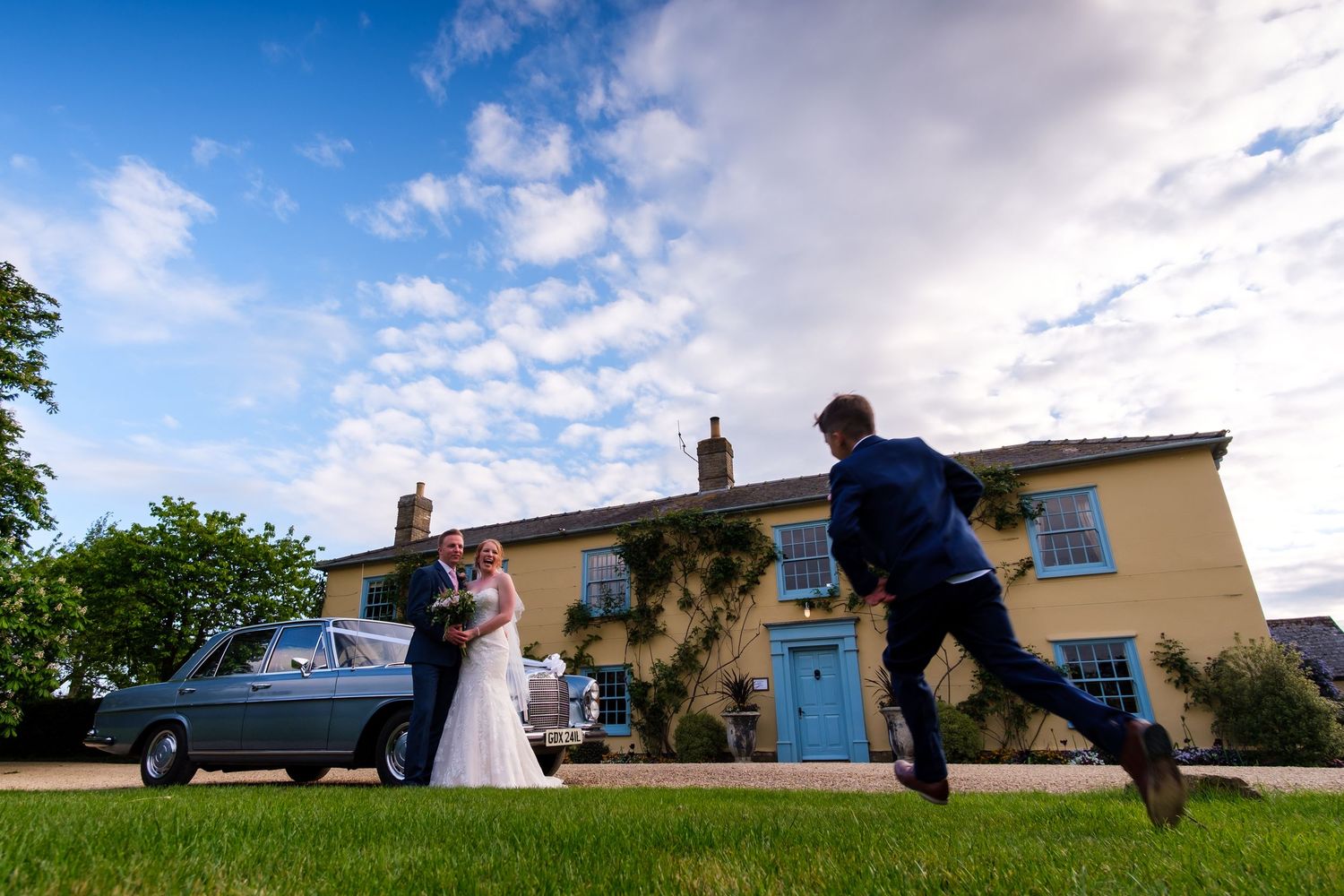 Wedding couple and guests running and playing on a grassy hill near a countryside house.