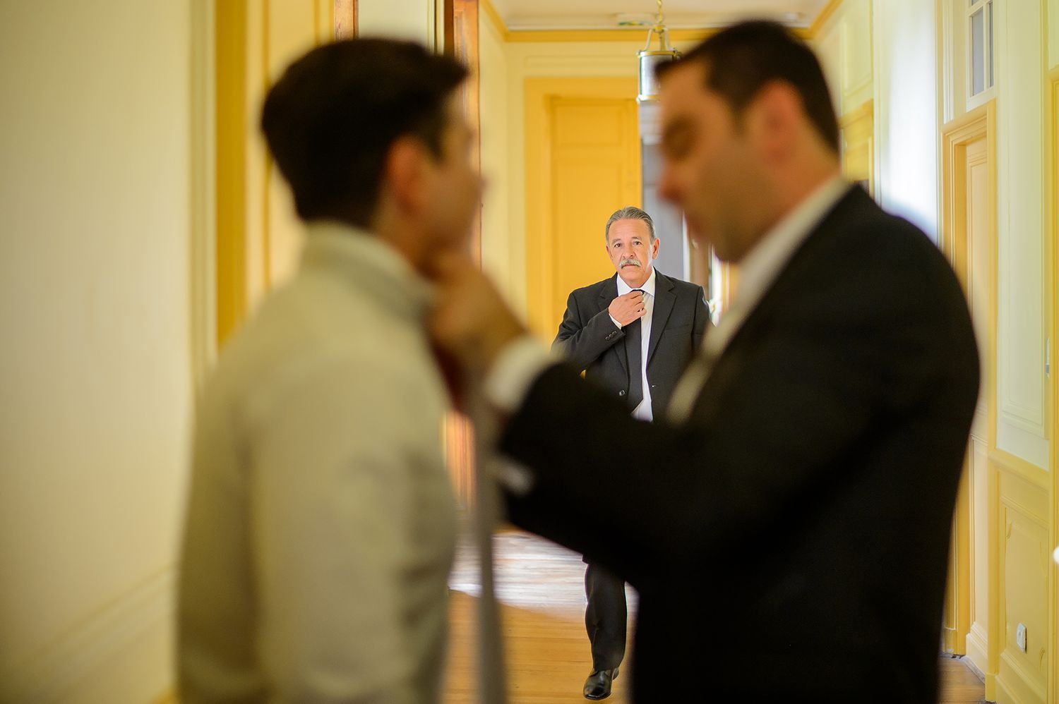Wedding guests walking and chatting in an elegant yellow-walled corridor.