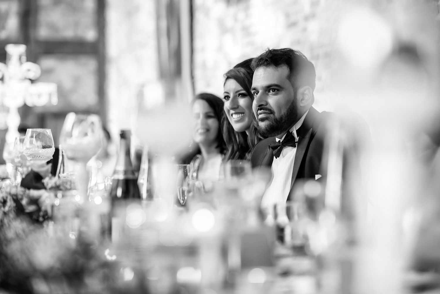 Wedding guests seated at tables during a reception in an elegant venue with exposed brick walls.