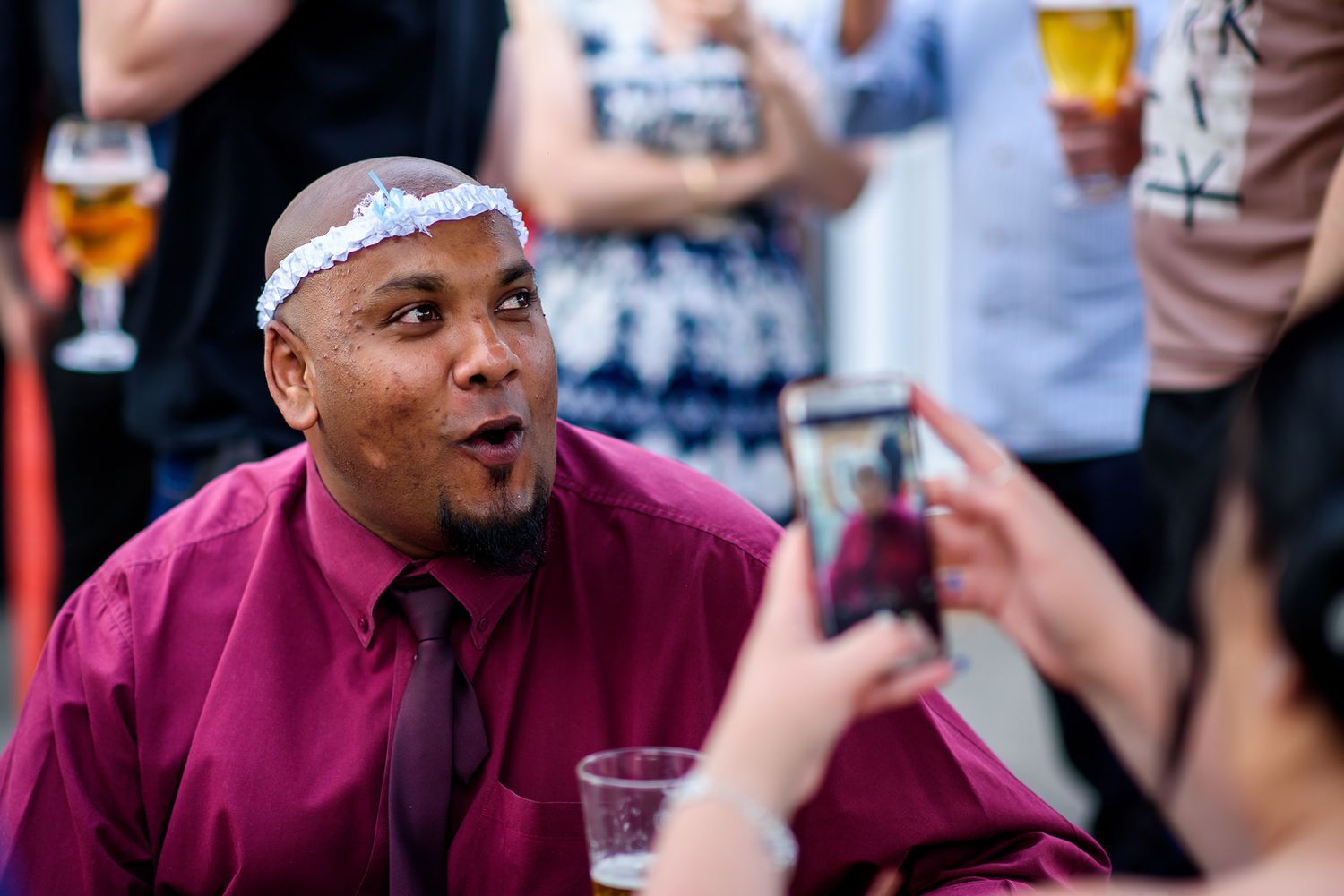 Wedding guests in burgundy shirts laugh and celebrate during outdoor reception.