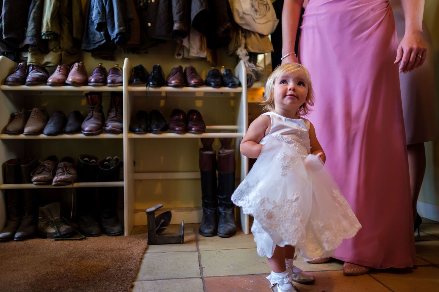 A little flower girl carries a basket while wearing a white dress and walking through a store filled with shoes.