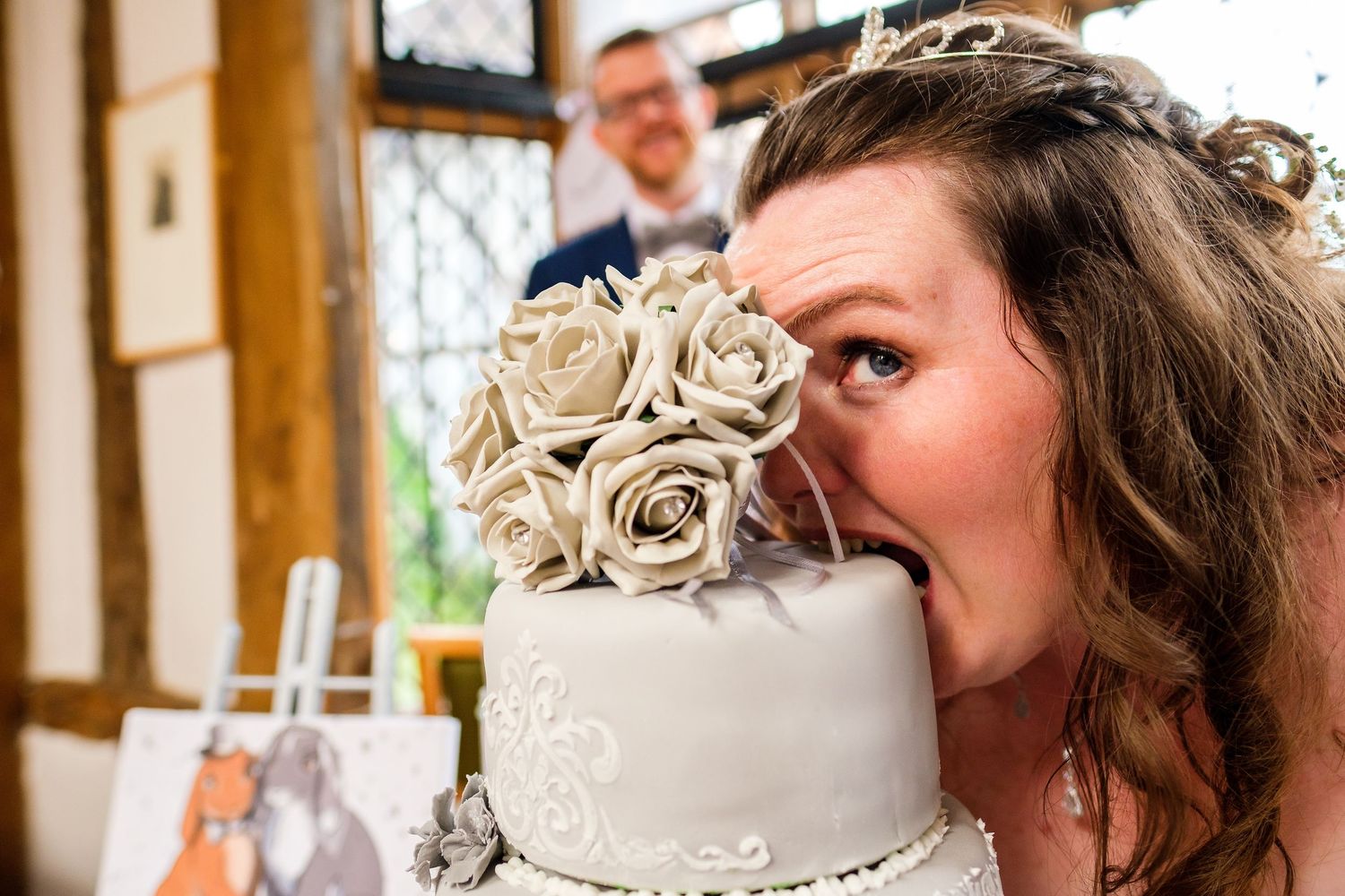 Close-up of someone playfully biting the wedding cake decorated with white roses.