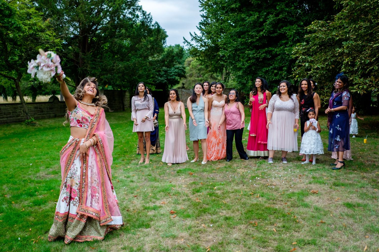 Wedding guests in colorful dresses gather on grassy lawn during outdoor celebration.
