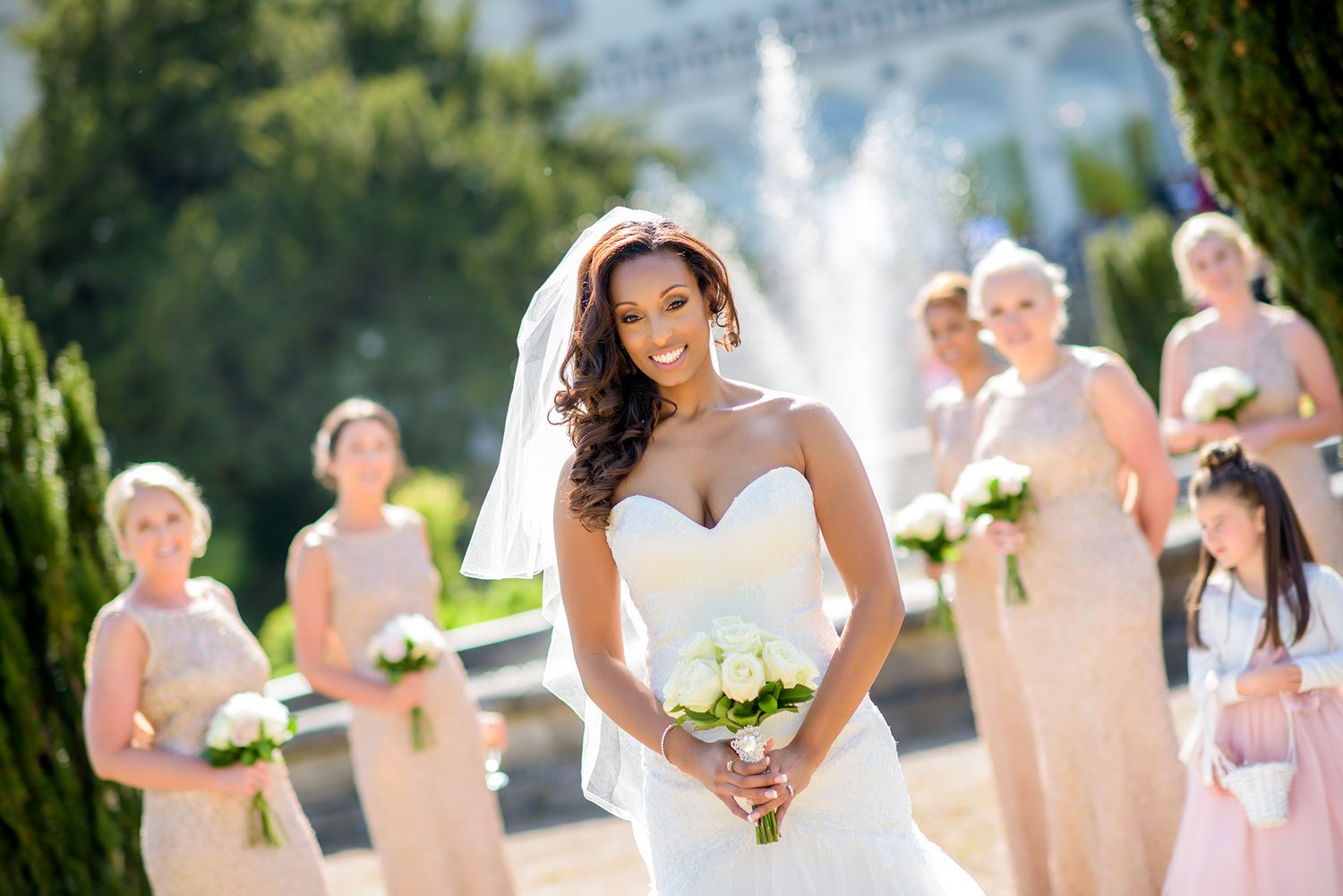 Bridal party in light dresses posing in sunny garden setting.