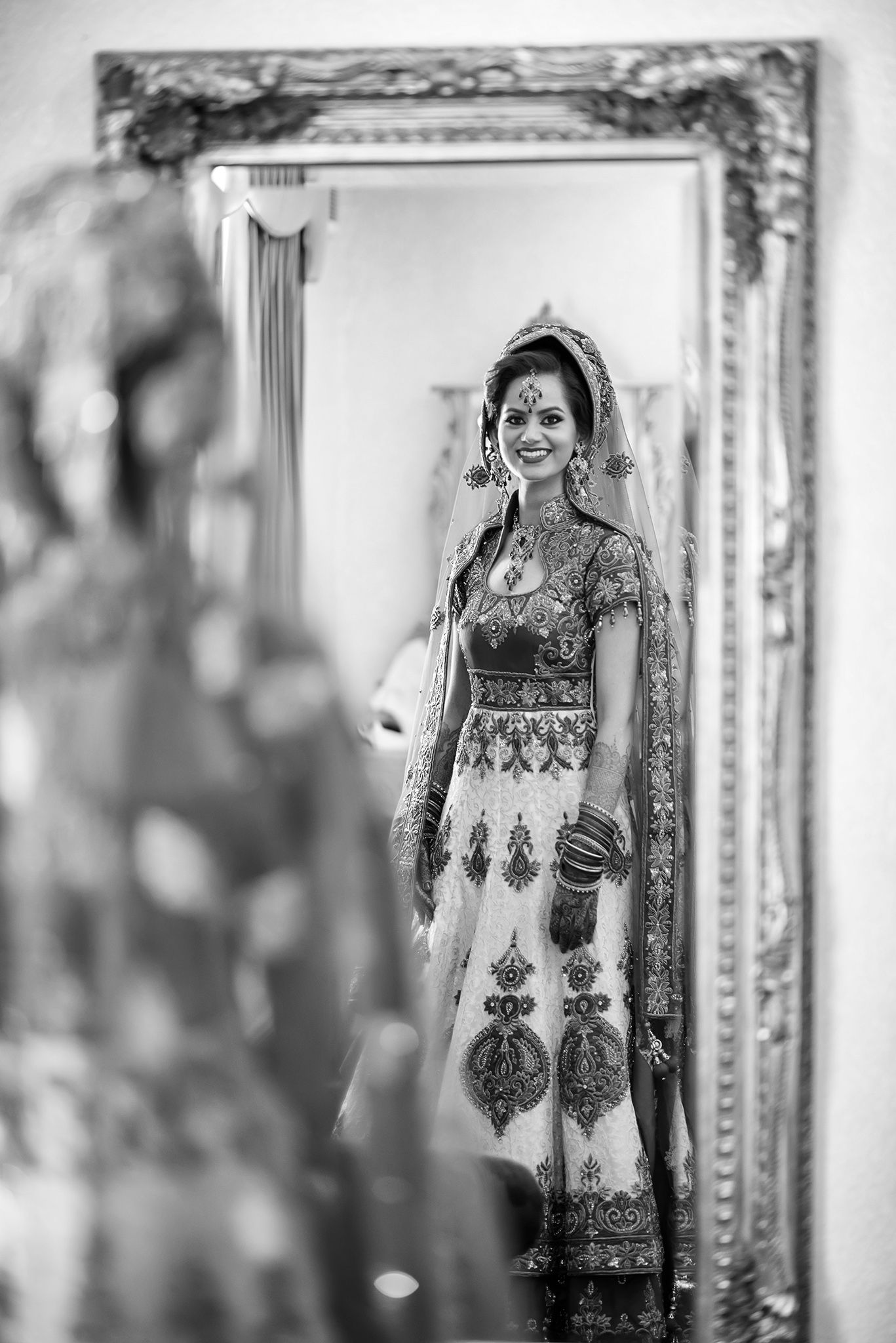 A reflection in an ornate mirror shows traditional bridal attire in black and white.