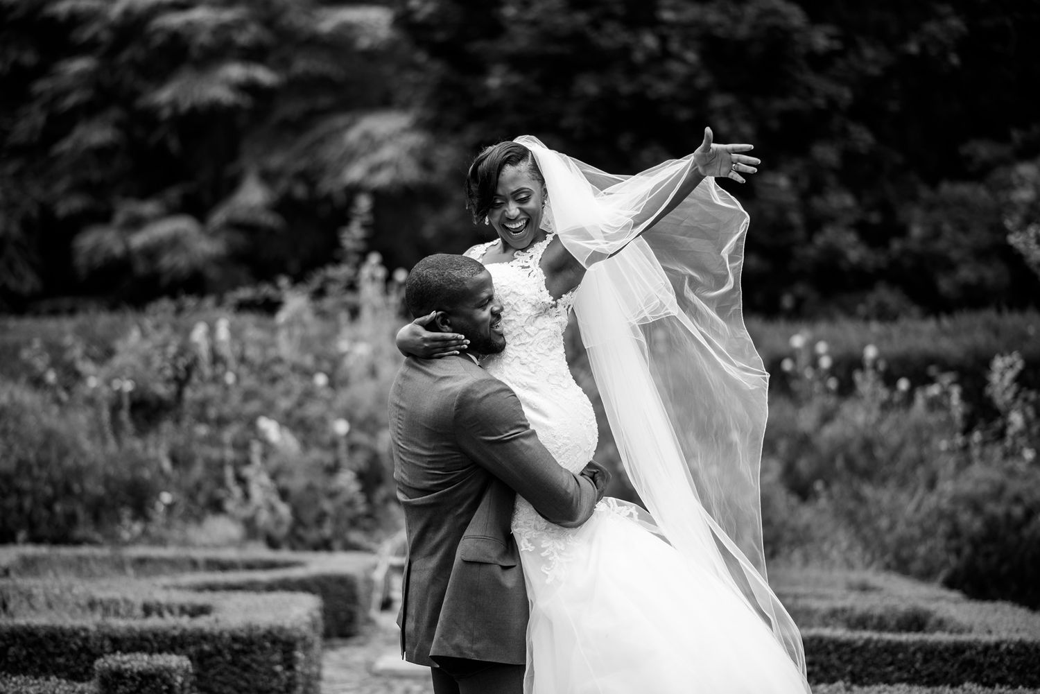 Wedding party members dance and celebrate joyfully in an outdoor garden setting.
