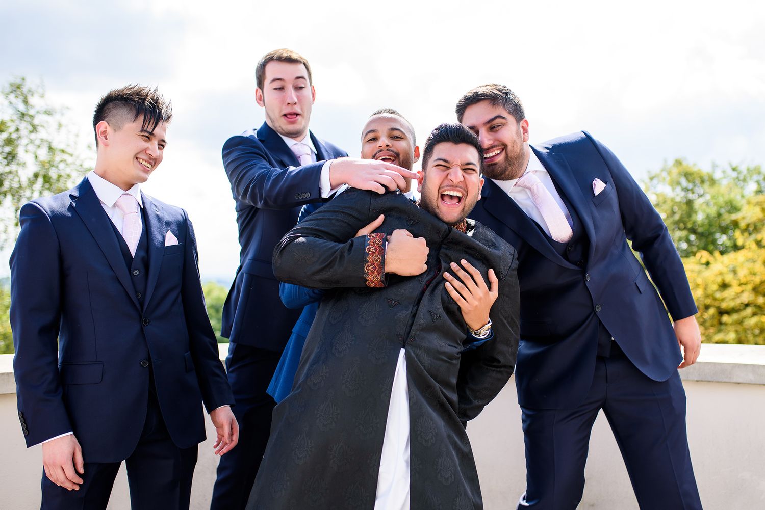 Groomsmen in navy suits posing playfully outdoors for wedding photos.