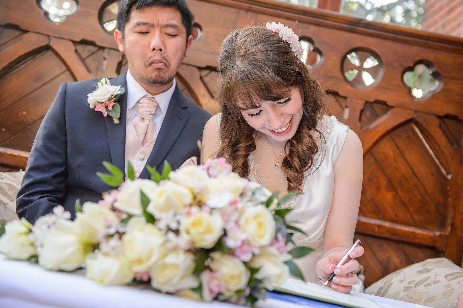A couple signs their marriage certificate at a ceremony with elegant floral decorations in a church setting.