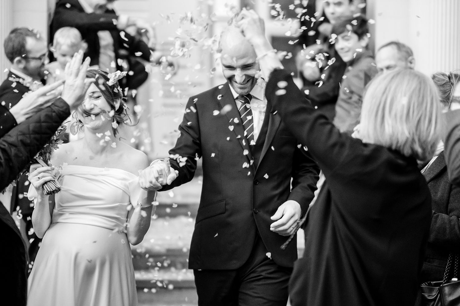 Black and white photo of wedding guests celebrating with confetti indoors.
