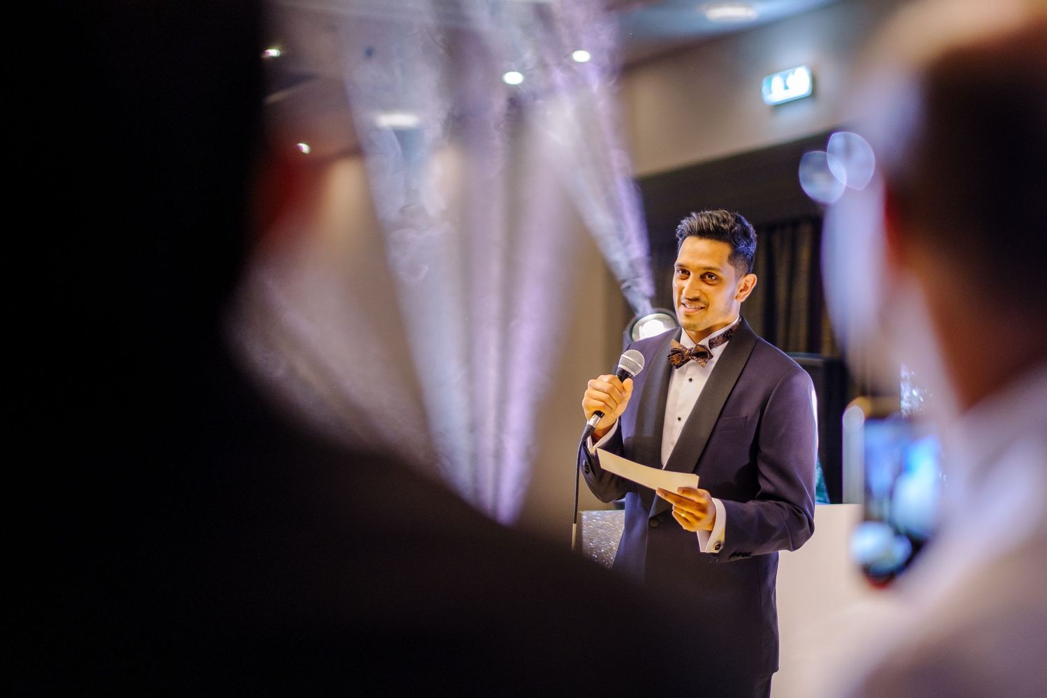 Wedding reception speech captured in dramatic lighting with purple spotlights.