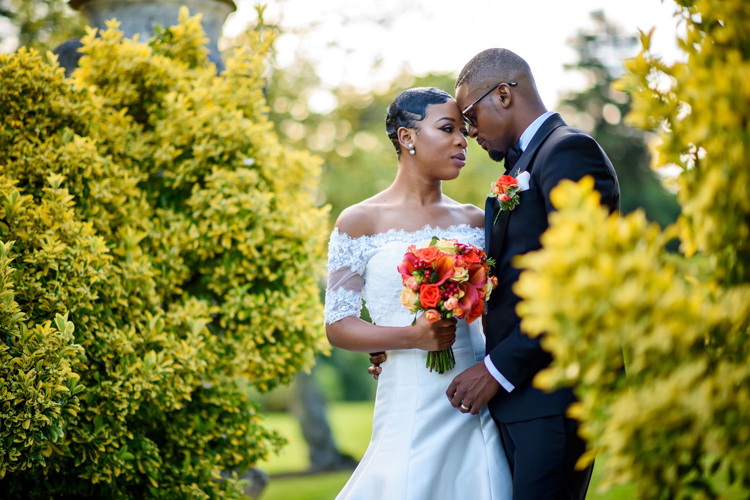 Wedding couple shares romantic moment among golden sunlit trees with red bouquet.