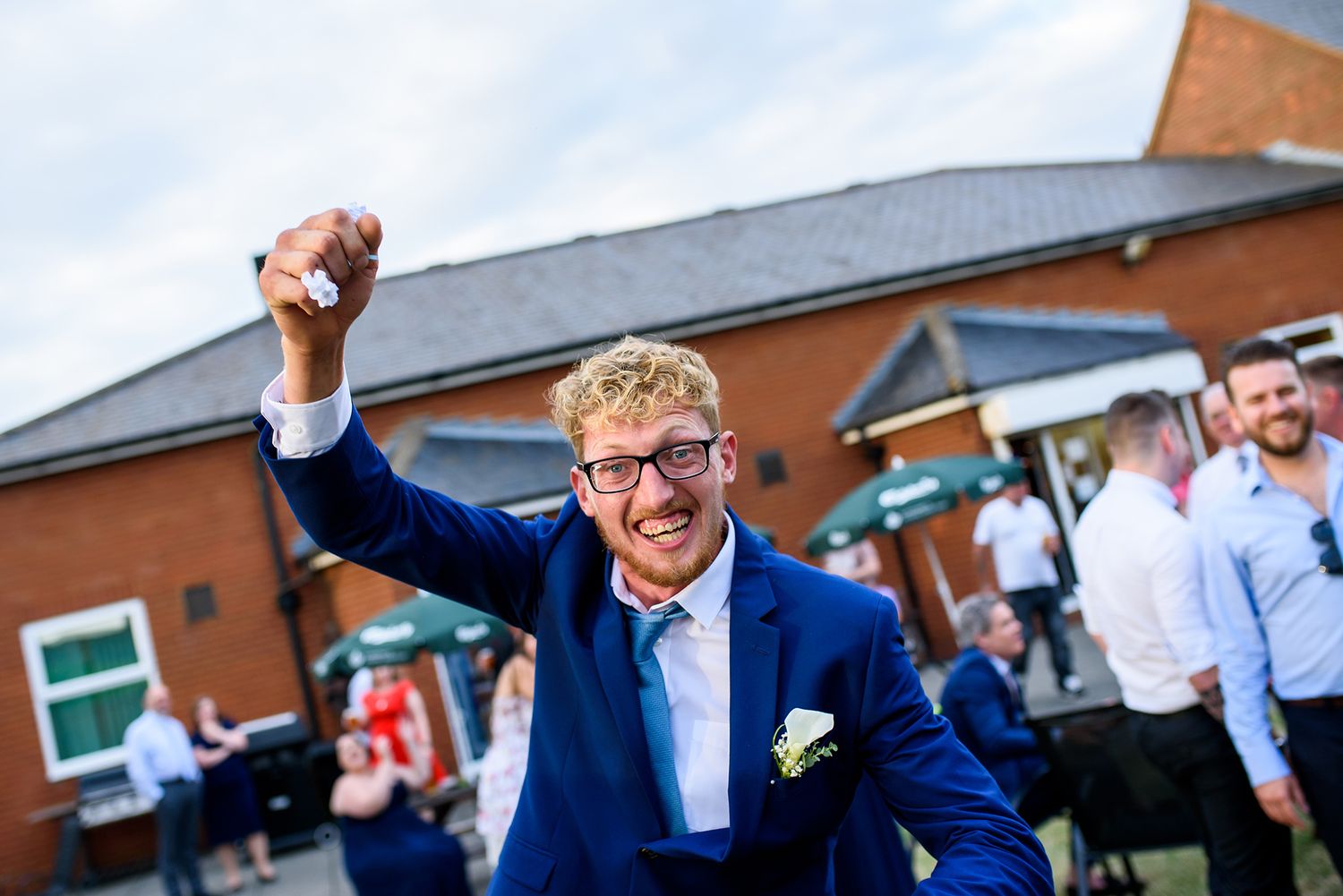 People dance joyfully at an outdoor wedding reception in front of brick buildings.