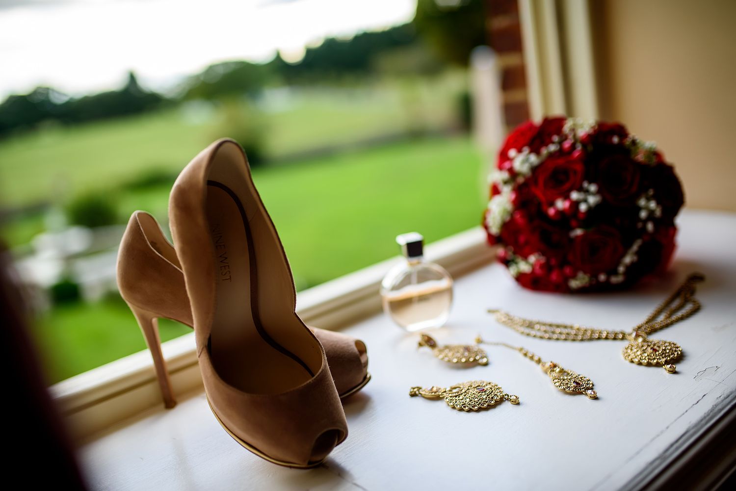 Brown high heel shoes and a red bouquet displayed against a blurred green background for a wedding detail shot.