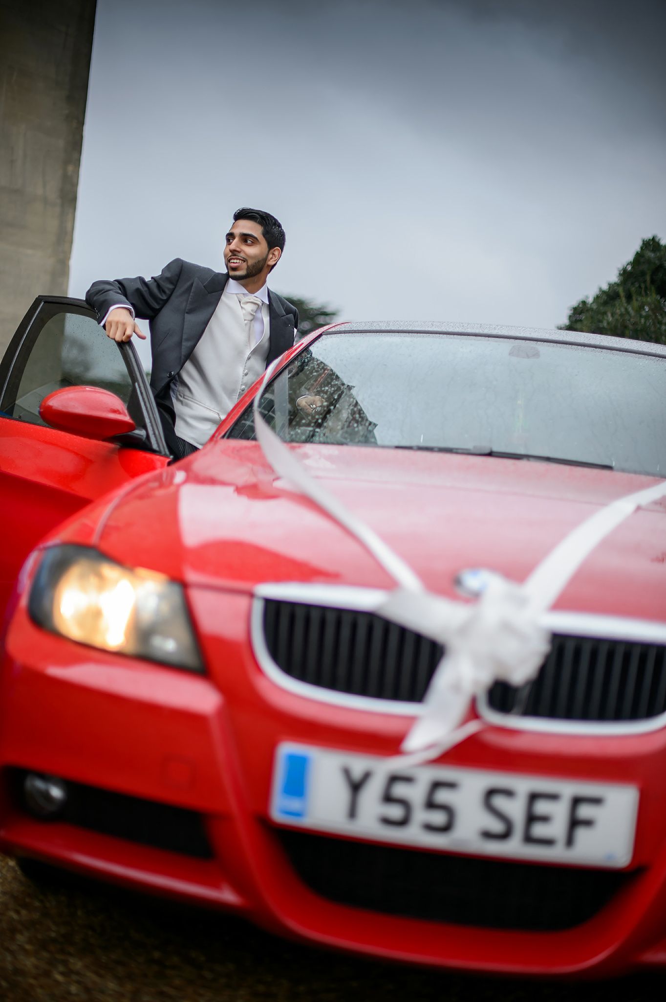 Red BMW car decorated with white ribbons for wedding transportation.