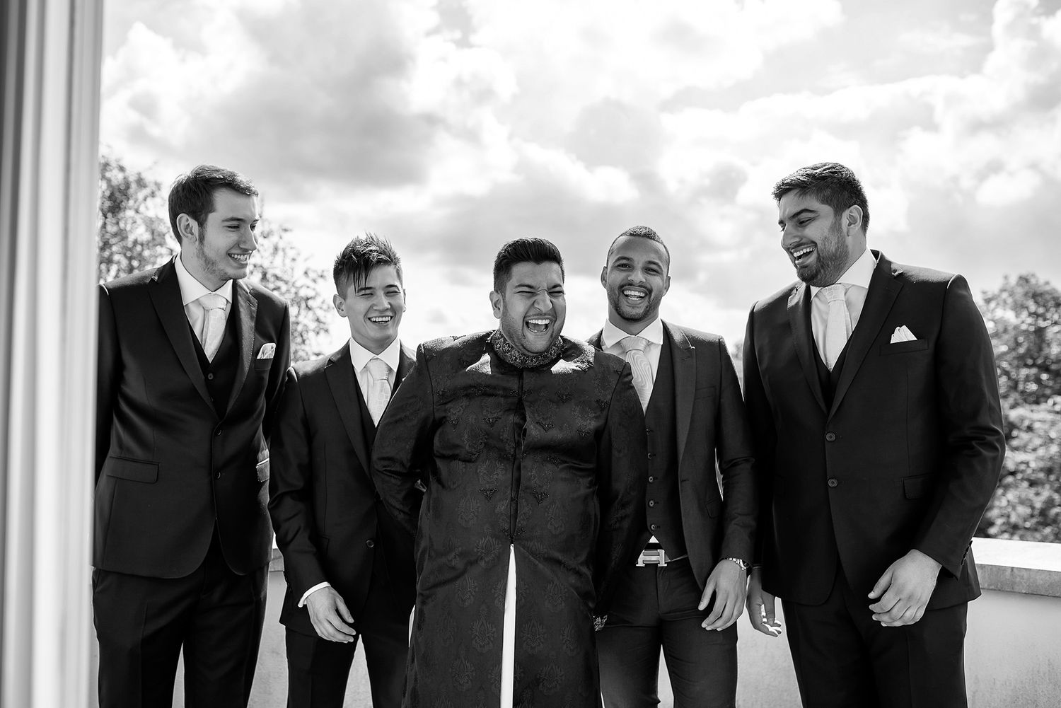 Black and white photo of groomsmen laughing together outdoors.