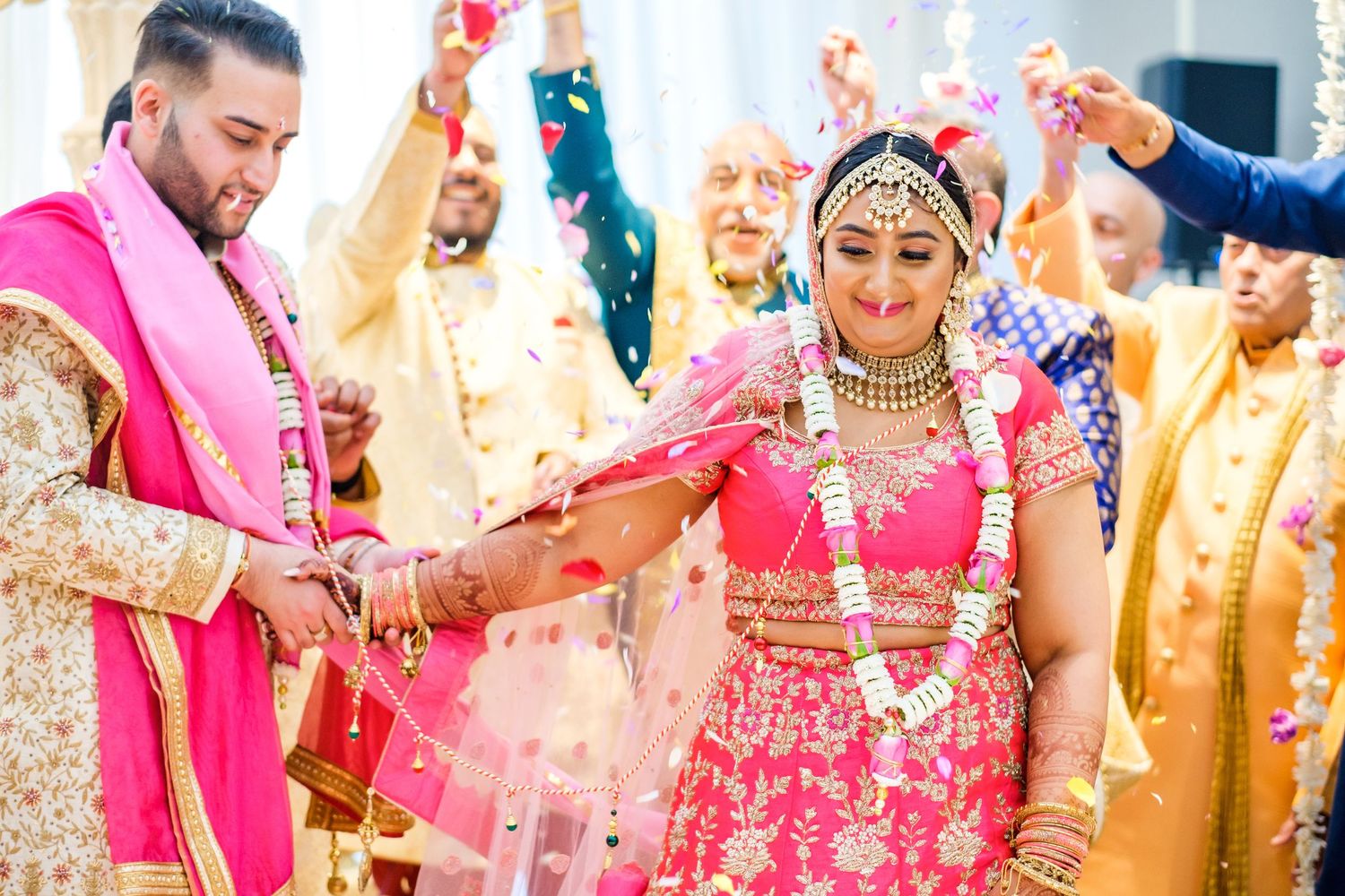 Celebratory moment during Indian wedding ceremony with pink attire and shower of flower petals.