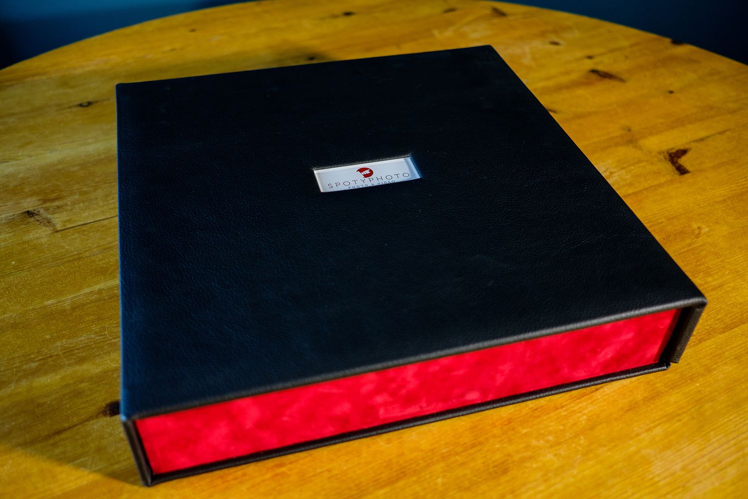 Premium black photo album with red accent displayed on wooden table surface.