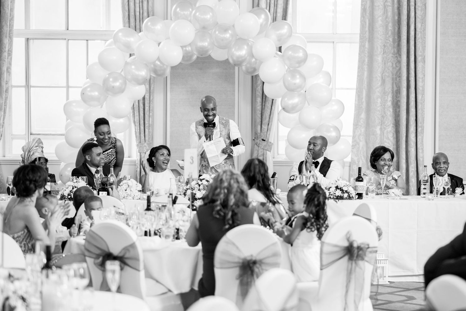 Elegant white balloon arch decorations at wedding reception venue with guests seated at tables.